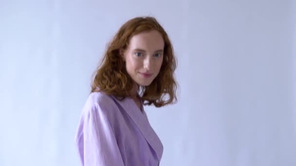 Весела позитивна дівчина позує на камеру в фіолетовому костюмі на білому тлі — стокове відео