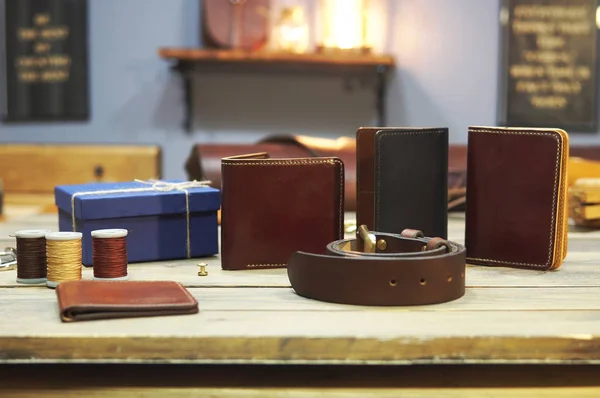 composition of different hand made leather man accessories on wooden background. Wallet, belt, purse, gift box, thread on wooden table