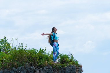 Kadın gezgin bir uçurumun kenarında duran ve okyanus manzarası keyfi bir sırt çantası ile. Bali, Endonezya. Seyahat ve aktif yaşam tarzı kavramı
