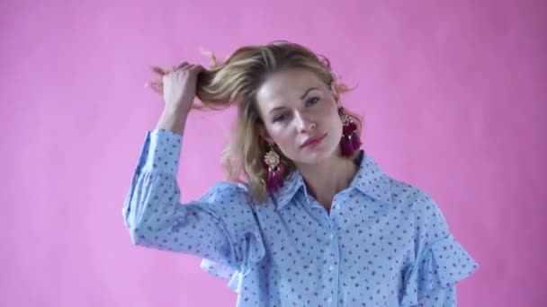 Весела позитивна блондинка позує на камеру на фотостудії на рожевому фоні — стокове відео