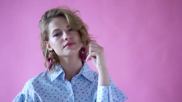 Весела позитивна блондинка позує на камеру на фотостудії на рожевому фоні — стокове відео