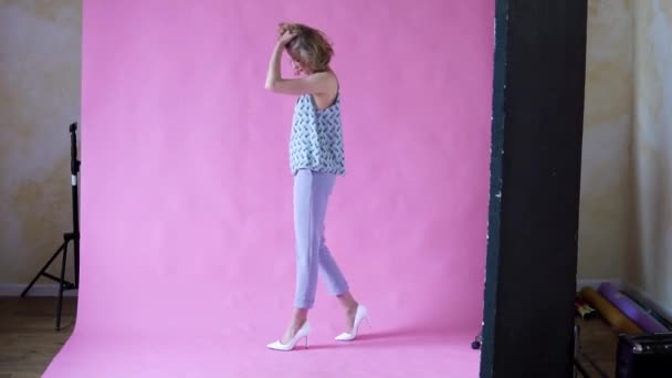 Vrolijke positieve blond meisje poseren voor de camera in een foto Studio op een roze achtergrond — Stockvideo