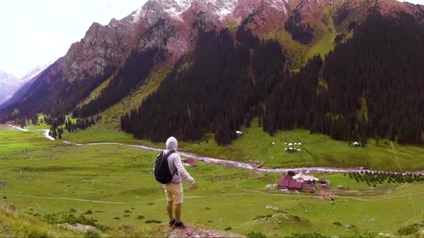 Ein junger Reisender mit Rucksack steht am Rande der Schlucht der Berge und schaut sich um — Stockvideo