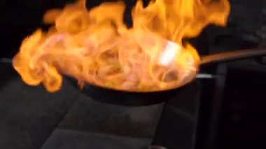 Aşçı lokanta mutfağında yemek pişiriyor ve ateş yakıyor.