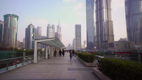 Shanghai, China - 15 de enero de 2018: Rascacielos de la zona de Pudong contra el cielo azul. Vista desde el puente peatonal por el que camina la gente — Vídeos de Stock