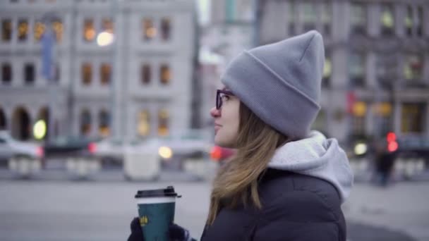 Een jong meisje in een zwarte jas en hoed loopt rond het prachtige Shanghai met koffie in haar handen — Stockvideo