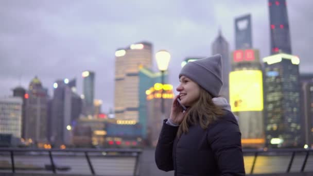 Een jong meisje in een zwarte jas en muts ontspannen wandelingen tijdens het praten over de telefoon — Stockvideo