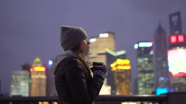 Een jong meisje in een zwarte jas en hoed loopt rond het prachtige Shanghai met koffie in haar handen — Stockvideo