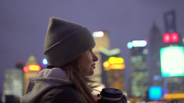 Une jeune fille dans une veste noire et chapeau se promène autour de la belle Shanghai avec du café dans ses mains — Video