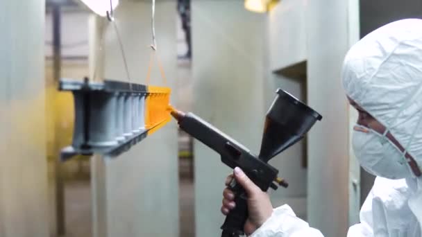 Recubrimiento en polvo de piezas metálicas. Un hombre con un traje protector rocía pintura en polvo de una pistola sobre productos metálicos — Vídeo de stock