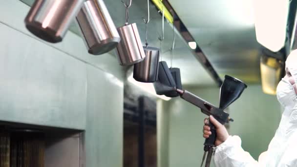 Revêtement en poudre de pièces métalliques. Un homme en combinaison de protection pulvérise de la peinture en poudre d'un pistolet sur des produits métalliques — Video