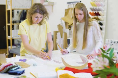 İki kadın moda tasarımcısı atölyede birlikte çalışıyorlar. Elbise dikmek için. Yeni tasarımlar üzerinde beyin fırtınası yapıyorlar..