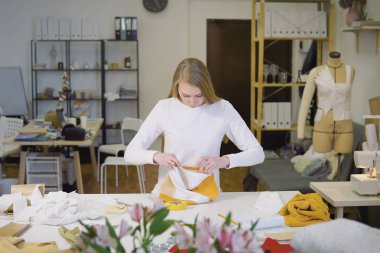 Sarışın bir kadın, serbest çalışan, moda tasarımcısı ya da atölyede renkli kumaşlarla tasarım ya da taslak üzerinde çalışan bir terzi. Ön görünüm