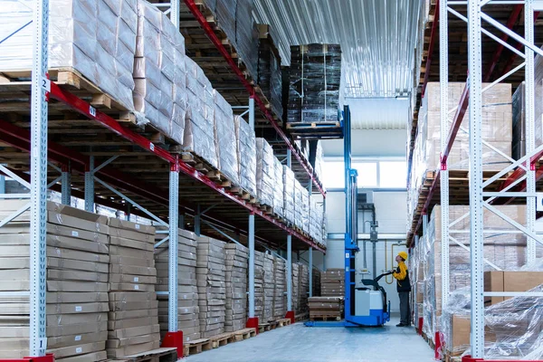 Üniformalı depo işçisi forklift yükleyicisiyle karton kutular yüklüyor.