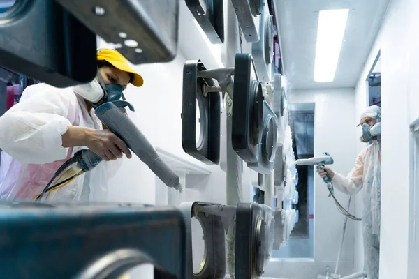 Recubrimiento en polvo de piezas metálicas. Hombre y mujer en traje protector pulveriza pintura en polvo blanco de pistola sobre productos metálicos — Foto de Stock