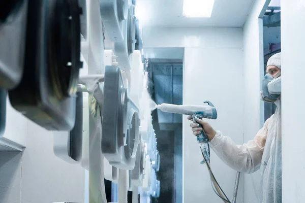 Powder coating of metal parts. Man in a protective suit sprays white powder paint from a gun on metal products — Stock Photo, Image