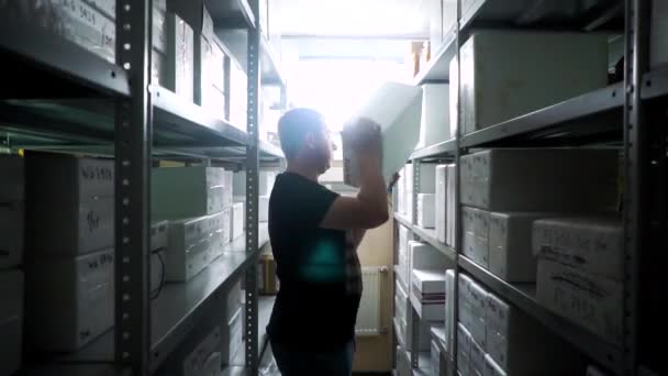 Trabajador del almacén pone o saca una caja del estante en un pequeño almacén — Vídeos de Stock