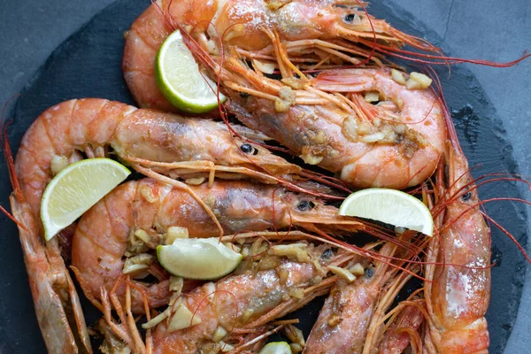 Gambones fritos con lima y ajo en un plato negro — Foto de Stock