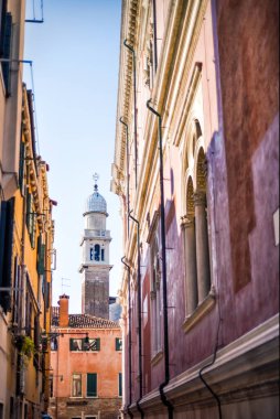 Venedik 'te arka planda kulesi olan dar bir sokak. Evler arasında küçük bir patika, birkaç metre. Venedik, İtalya seyahatleri ve güneşli bir günde turizm merkezi. Venedik sularındaki ünlü İtalyan şehri.