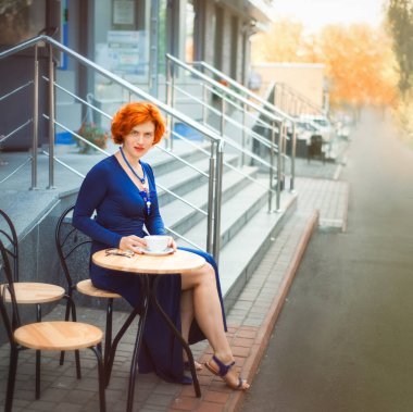 Güzel, kızıl saçlı, 30 yaşında bir kadın bir fincan kahveyle kafede oturuyor. Yaz günü kendine vakit ayır. Modern sokak restoranında sabah çayı ya da kahve..