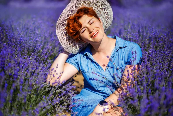 短い散髪と青いドレスとラベンダー畑で暑い夏の日に座ってわら帽子で目を閉じた幸せな赤い髪の女性 プロヴァンスの田舎の夏 — ストック写真