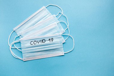 Mavi arka planda COVID-19 yazılı tıbbi yüz maskeleri. Coronavirus enfeksiyonu önleme konsepti