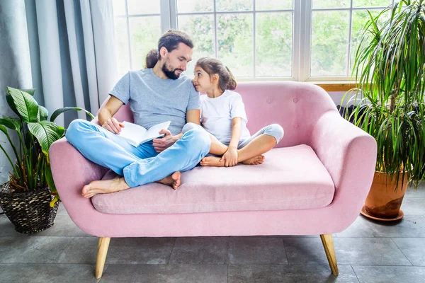 Fathers day concept. Amazing father and cute little girl reading a book, smiling and enjoying at home. Happy parenthood. Father and daughter spending time together.