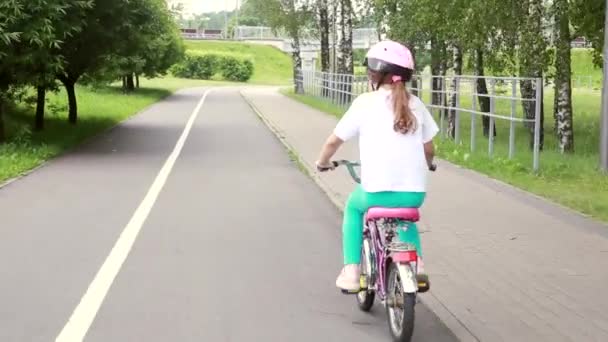 Sport kislány egy védő sisakban biciklizik egy kerékpárúton a parkban. Outboor nyári gyermekprogramok és egészséges családi koncepció. — Stock videók