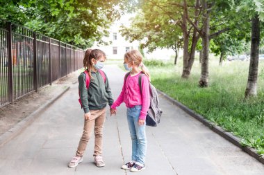 Covid-19 salgını sırasında okula dönen iki kız. Okulda koruyucu yüz maskesi takan okul çocuğu..