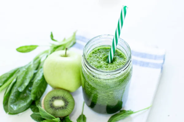 Smoothie verde saludable con espinacas en una taza con una tira de tela de lino sobre un fondo de mesa blanco —  Fotos de Stock