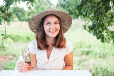 Gülümseyen mutlu genç kadın dışarıda bir kadeh şarapla eğleniyor ve dinleniyor. Boş zaman..