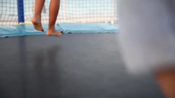 Jungen und Mädchen haben Spaß beim Sommerurlaub auf See. Nahaufnahme der Beine von zwei Kindern, die während des Sonnenuntergangs auf einem Trampolin am Strand springen. Kindheit und aktiver Lebensstil in der Familie. — Stockvideo