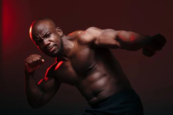 Un luchador etíope musculoso se para en una pose de boxeo y hace un disparo hacia la cámara en luz roja . — Foto de Stock
