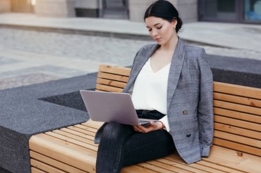 Bir iş kadını dizüstü bilgisayarını kucağında tutuyor ve mola sırasında sokakta otururken son haberleri izliyor..