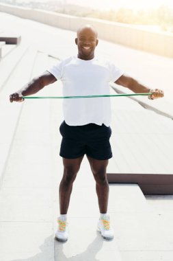 Siyah atlet sokakta elastik spor bandıyla antrenman yapıyor. Göğüs seviyesine bir bant genişletici gerin.