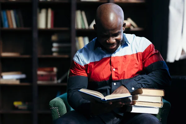 Estudante negro afro-americano em um blusão esportivo estuda e lê livros na biblioteca, preparando-se para o exame . — Fotografia de Stock