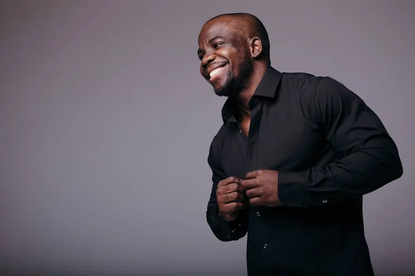 Africano calvo divertido hombre sonríe y botones de su camisa y mira hacia el futuro. Un hombre con una camisa negra . — Foto de Stock