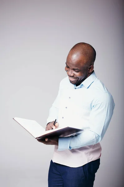 Foto vertical trabalhador de escritório africano em camisa branca folheando através de um livro grosso e sorrindo — Fotografia de Stock