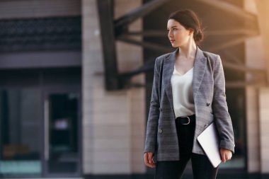 Elinde dizüstü bilgisayar tutan güzel bir iş kadını. Uçakta bir gökdelen var.