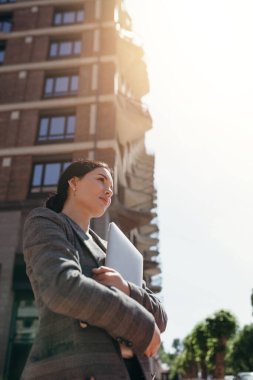 Dizüstü bilgisayarını elinde tutan güzel bir iş kadınının alt görüntüsü. Uçakta bir gökdelen var.