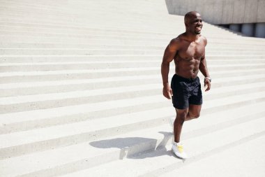 Çıplak gövdeli, şortlu, uzun sokak aktiviteleri için parktaki merdivenlerden inen siyah bir adam.