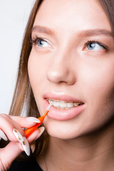 Лицо красивой девушки с брекетами на зубах, которая чистит зубы и брекеты от еды щеткой — стоковое фото