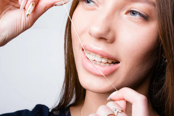 Крупный план лица улыбающейся девушки с брекетами на зубах, которая чистит зубы нитью после того, как ест зубную нить — стоковое фото