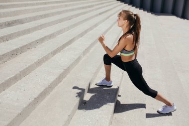 Pilates antrenörü egzersiz yapıyor ve parkta merdivenlerde iç bacak kasları geliştiriyor.
