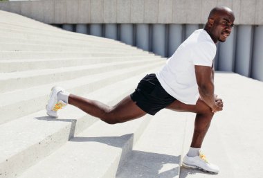 Beyaz futbol ve siyah şortlu atletik siyah antrenör parktaki merdivenlerde dizine yaslanarak öne atlıyor.