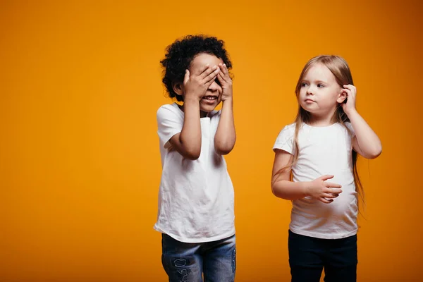 En pojke och en flicka av olika nationaliteter i vita t-shirts leker kurragömma tillsammans. Barn har inte rasism — Stockfoto