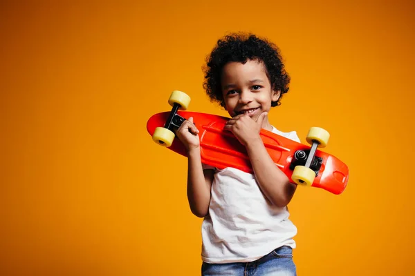 African American Boy en T-shirt blanc et jeans étreint une planche à roulettes rouge et la presse sur sa poitrine . — Photo