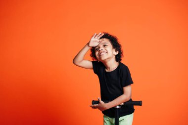 Siyah çocuk scooter 'a biner ve uzaktan bakarken avucunu yana doğru bastırır. Çocuksu mutluluk kavramı