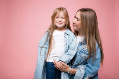 Güzel anne küçük kızını elinden tutar ve ona bakar. Pembe arkaplan