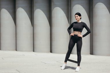 Ayak bileklerinde spor lastiğiyle egzersiz yapan bir pilates eğitmeninin uzun bir portresi bacak kaslarını güçlendirmek için..